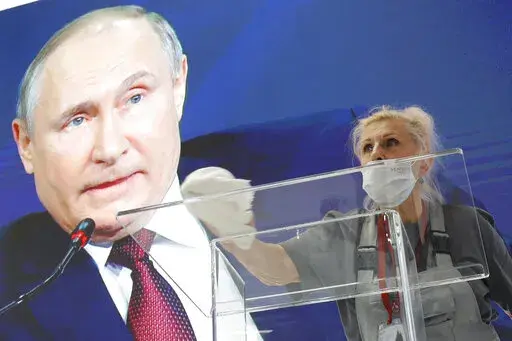 A worker cleans a speaker's podium as Russian President Vladimir Putin seen on a screen in the background at the St. Petersburg International Economic Forum in St. Petersburg, Russia, June 4, 2021. Russia’s showpiece investment gathering begins Thursday, June 16, 2022 and organizers are telling foreign participants to be sure to bring cash — not necessarily for making investments, but for spending money. The advice for the St. Petersburg International Economic Forum is a quiet acknowledgment