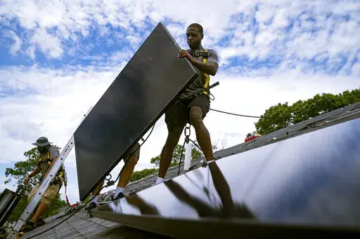 Employees of NY State Solar, a residential and commercial photovoltaic systems company, install an array of solar panels on a roof, Aug. 11, 2022, in the Long Island hamlet of Massapequa, N.Y. Massive incentives for clean energy in the U.S. law signed Tuesday, Aug. 16, by President Joe Biden should reduce future global warming “not a lot, but not insignificantly either,” according to a climate scientist who led an independent analysis of the climate package.  (AP Photo/John Minchillo, File)