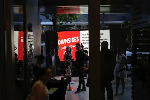 Staff and guests stand at the entrance to a pop-up tasting event for "lab-grown" meat produced by Upside Foods, as a protest truck parked out front displays a message advocating against cultivated meat, Thursday, June 27, 2024, in Miami. As Florida's ban on lab-grown meat is set to go into effect next week, one manufacturer hosted a tasting party, serving up cultivated chicken tostadas to dozens of attendees on a rooftop in Miami's Wynwood neighborhood. (AP Photo/Rebecca Blackwell)