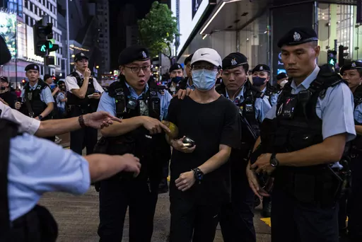 A member of the public is escorted by police after shining the light from a smartphone, near Victoria Park, the city's venue for the annual 1989 Tiananmen massacre vigil, on the 34th anniversary of China's Tiananmen Square crackdown in Hong Kong, Sunday, June 4 2023. (AP Photo/Louise Delmotte)