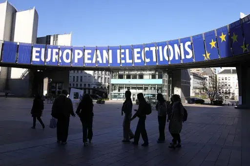 A group stands under an election banner outside the European Parliament in Brussels on April 29, 2024. In an increasingly vitriolic political climate, the last thing needed in the runup to the June European Union elections was an assassination attempt on one of the bloc’s most controversial figures. (AP Photo/Virginia Mayo, File)