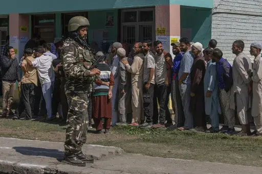 An Indian paramilitary soldier stands guard as people queue up at a polling booth to cast their vote in Bellow, south of Srinagar, Indian controlled Kashmir, Wednesday, Sept. 18, 2024. (AP Photo/Dar Yasin)