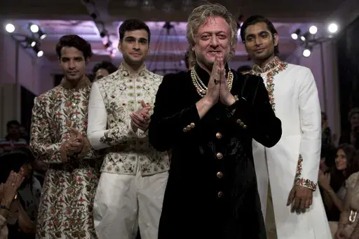 Fashion designer Rohit Bal, foreground, acknowledges the applause next to models wearing his creations at the end of his show at the Couture Week 2016 in New Delhi, India, Sunday, July 24, 2016. (AP Photo/Tsering Topgyal, File)