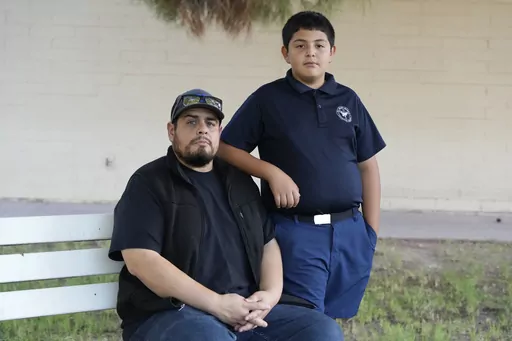 Aaron Galaz and his son pose for a photo on Wednesday, Oct. 18, 2023 in Phoenix. Aaron Galaz said his son is enrolled in a program that uses taxpayer funds to pay for private-school tuition in part so his son could be challenged more in class. At least four states that have made most children eligible for taxpayer-funded scholarships to private schools are seeing more families using the programs than planned. That could cost taxpayers, but it's early to know the exact budget implications. (AP Ph