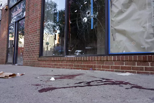 ADDS CONTEXT AND DETAIL THAT THESE BULLET HOLES ARE FROM A PRIOR SHOOTING - Blood is seen at the scene of a fatal overnight shooting on South Street in Philadelphia, Sunday, June 5, 2022, where bullet holes on a storefront window from a prior shooting can also be seen. (AP Photo/Michael Perez)