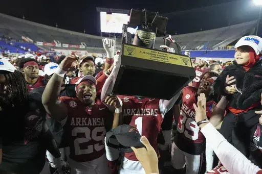 Arkansas players raise the trophy as they celebrate after winning the Liberty Bowl NCAA college football game against Texas Tech, Friday, Dec. 27, 2024, in Memphis, Tenn. (AP Photo/George Walker IV)