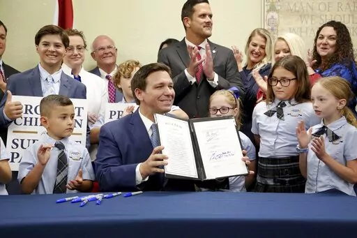 Florida Gov. Ron DeSantis displays the signed Parental Rights in Education, aka the Don't Say Gay bill, flanked by elementary school students during a news conference on Monday, March 28, 2022, at Classical Preparatory school in Shady Hills. (Douglas R. Clifford/Tampa Bay Times via AP)