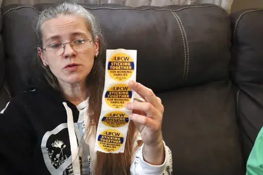 Former Tudor's Biscuit World employee Jennifer Patton, 38, holds up stickers displaying the logo of the United Food & Commercial Workers Local 400 union at her coworker's home in Elkview, W.Va., on Jan. 20, 2022. Patton said she was retaliated against and fired by management after she joined efforts to unionize the restaurant. Employees at the Elkview, W.Va., restaurant have already case ballots to decide whether or not they want to create a union. The votes will be read Tuesday. (AP Photo/Leah 