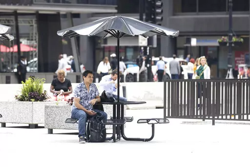 A person sits at a table at Daley Plaza in the loop, Monday, June 13, 2022, in Chicago. (Ashlee Rezin/Chicago Sun-Times via AP)