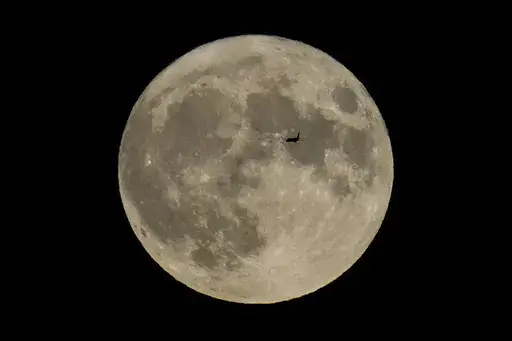 A plane passes in front of the moon, Aug. 30, 2023, in Chicago. Scientists have confirmed a cave on the moon, not far from where Neil Armstrong and Buzz Aldrin landed 55 years ago this week, and suspect there are hundreds more that could house future astronauts. (AP Photo/Kiichiro Sato, file)