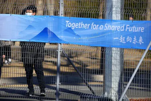A person looks through the fence at the closed-loop area for Olympics personnel on the Olympic Green near at the 2022 Winter Olympics, Tuesday, Feb. 1, 2022, in Beijing. (AP Photo/Mark Schiefelbein, File)