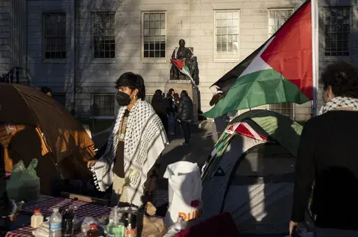A student protester stands in front of the statue of John Harvard, the first major benefactor of Harvard College, draped in the Palestinian flag, at an encampment of students protesting against the war in Gaza, at Harvard University in Cambridge, Mass., April 25, 2024. (AP Photo/Ben Curtis, File)