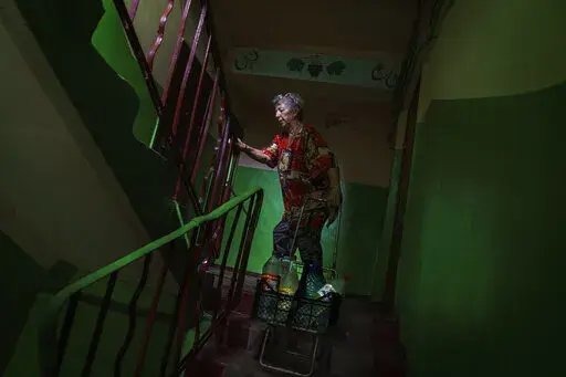 Lyubov Mahlii, 76, pulls a crate of water bottles up the stairs to her fifth floor apartment after filling them up at a nearby park in Sloviansk, Donetsk region, eastern Ukraine, Saturday, Aug. 6, 2022. A lack of running water in the city means that residents must fill bottles by hand at public pumps. While the remaining population has adapted to this new way of life, local officials warn that the coming of winter could set the stage for a humanitarian crisis. (AP Photo/David Goldman)
