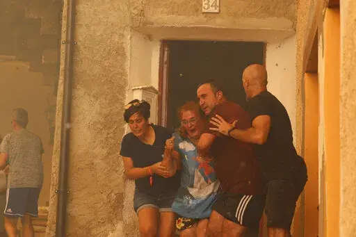 A woman is helped out of a house by neighbours in Anon de Moncayo, Spain on Saturday Aug. 13, 2022. A large wildfire in northeast Spain grew rapidly overnight and was burning out of control. It has already forced the evacuation of eight villages and 1,500 people in Zaragoza province. A local government official said Sunday that the situation was critical in the town of Añon de Moncayo and the priority for the 300 firefighters fighting the blaze was to protect human lives and villages. (Fabian S