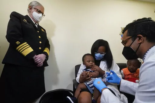 Pediatrician Emy Jean-Marie, center, holds her nine-month-old son Adedeji Adebayo, Emiola Adebayo, 3, on her lap as Dr. Nizar Dowla, right, administers a vaccine while        Department of Health and Human Services Assistant Secretary for Health, Admiral Rachel Levine, left, looks on, Tuesday, June 28, 2022, at the Borinquen Health Care Center in Miami. Florida is the only state that didn't pre-order the under-5 vaccine, and state Surgeon General Joseph Ladapo has recommended against vacci