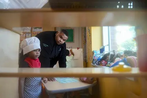 Leading Men fellow Davontez Johnson, right, interacts with a preschooler playing dress-up during choice time, a classroom period where children can choose their own activities, Thursday, Oct. 3, 2024, at Dorothy I. Height Elementary School in Baltimore. (AP Photo/Stephanie Scarbrough)