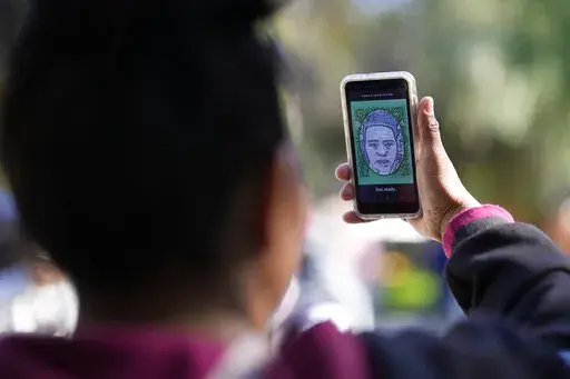 A migrant from Michoacan, Mexico, uses the CBPOne app Tuesday, Jan. 24, 2023, in Tijuana, Mexico. A mobile app for migrants to seek asylum in the United States has been oversaturated since it was introduced this month in one of several major changes to the government's response to unprecedented migration flows. Hoping to get lucky when a new appointments are made available daily, migrants are increasingly frustrated by a variety of error messages. (AP Photo/Gregory Bull)