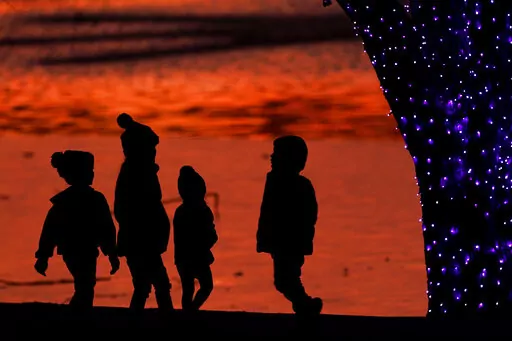 In this Dec. 26, 2020 file photo, children are silhouetted against a pond as they look at Christmas lights at a park in Lenexa, Kan. Custodial accounts are a way to invest for minors and give them a headstart on building wealth. How can you ensure they’re financially responsible enough to manage their assets when they reach the age of majority? One way is to share your money values with them and teach budgeting basics as well as saving tactics early on. (AP Photo/Charlie Riedel, File)