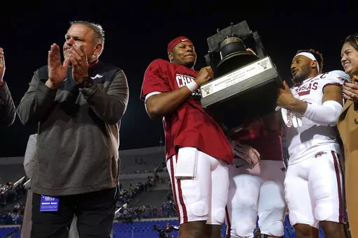 Arkansas coach Sam Pittman, left, applauds as quarterback KJ Jefferson, center, and defensive back Simeon Blair (15) attempt to hoist overhead the trophy following the team's win over Kansas in the Liberty Bowl NCAA college football game, Wednesday, Dec. 28, 2022, in Memphis, Tenn. Arkansas won 55-53 in three overtimes. (AP Photo/Rogelio V. Solis)