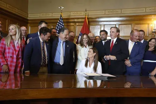Arkansas Gov. Sarah Huckabee Sanders signs tax cut bills from a special session while surrounded by state legislators, Wednesday, June 19, 2024, at the state Capitol in Little Rock, Ark. Huckabee Sanders on Wednesday signed legislation to cut the state's property and income taxes after lawmakers wrapped up a special session where they also approved legislation averting a shutdown of the state's hunting and fishing programs. (Thomas Metthe/Arkansas Democrat-Gazette via AP)