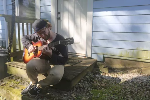 Camera assistant Alex Buhlig plays his guitar outside his Atlanta apartment on Oct. 18, 2023. With the actors' strike still ongoing and filming largely shut down, Buhlig has been teaching guitar lessons to make ends meet. (AP Photo/R.J. Rico)