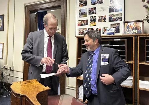 Mark Stewart Greenstein, right, hands a pen back to New Hampshire Secretary of State David Scanlan after filing to get on the state's 2024 Democratic presidential primary ballot on Wednesday, Oct. 11, 2023 in Concord, N.H. Greenstein, of West Hartford, Connecticut, is making his fourth long-shot bid for the nomination. (AP Photo/Holly Ramer)