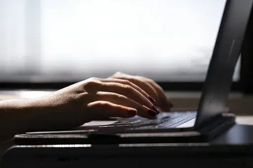 This May 18, 2021, photo shows a woman typing on a laptop on a train in New Jersey. Scams are common on peer-to-peer payment apps, but you can keep your money safe by avoiding questionable payment requests that may be fraudulent, only sending money to people you know and upgrading your privacy settings. While payment apps are convenient, they also carry risks if you use them without first vetting who exactly you are sending money to. (AP Photo/Jenny Kane, File)
