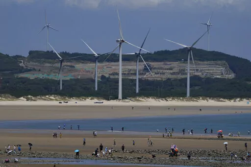 Beachgoers walk near wind turbines along the coast of Pingtan in Southern China's Fujian province, on Aug. 6, 2022. The world's two biggest emitters of greenhouse gases are sparring on Twitter over climate policy, with China asking if the U.S. can deliver on the landmark climate legislation signed into law by President Joe Biden this week. (AP Photo/Ng Han Guan)