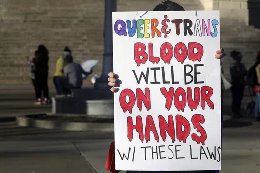 A protester outside the Kansas Statehouse holds a sign after a rally for transgender rights on the Transgender Day of Visibility, March 31, 2023, in Topeka, Kan. A new rule from President Joe Biden's administration assuring transgender students be allowed to use the school bathrooms that align with their gender identity could conflict with laws in Republican-controlled states that seek to make sure they can't. (AP Photo/John Hanna, File)