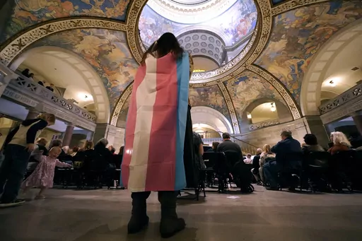 Glenda Starke wears a transgender flag as a counterprotest during a rally in favor of a ban on gender-affirming health care legislation, March 20, 2023, at the Missouri Statehouse in Jefferson City, Mo. Minors in Missouri soon will be required to undergo 18 months of therapy before receiving gender-affirming health care under an emergency rule released Thursday, April 13, 2023, by the state's Republican attorney general. (AP Photo/Charlie Riedel, File)
