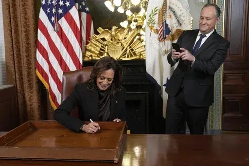 Vice President Kamala Harris, with second gentleman Doug Emhoff at right, signs the desk drawer in her ceremonial office as part of a long-standing tradition for Vice Presidents, in the Eisenhower Executive Office Building on the White House complex in Washington, Thursday, Jan. 16, 2025. (AP Photo/Susan Walsh)