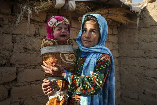 Qandi Gul holds her brother outside their home housing those displaced by war and drought near Herat, Afghanistan. Dec. 16, 2021. Gul’s father sold her into marriage without telling his wife, taking a down-payment so he could feed his family of five children. Without that money, he told her, they would all starve. He had to sacrifice one to save the rest. (AP Photo/Mstyslav Chernov)