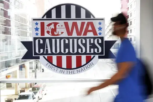 A pedestrian walks past a sign for the Iowa Caucuses on a downtown skywalk, in Des Moines, Iowa, on Feb. 4, 2020. (AP Photo/Charlie Neibergall, File)