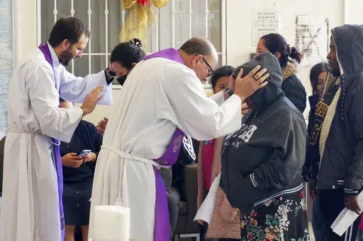The Rev. Brian Strassburger, left, and the Rev. Flavio Bravo, right, bless migrants during Mass at the Casa del Migrant shelter in Reynosa, Mexico, on Dec. 15, 2022. Both hope and tension have been rising here and the few other shelters in this border city where thousands of migrants await news of U.S. border policy changes possibly less than a week away. (AP Photo/Giovanna Dell'Orto)