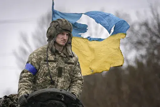 A Ukrainian serviceman is backdropped by his country's flag while standing on a tank, outside Kyiv, Ukraine, Saturday, April 2, 2022. As Russian forces pull back from Ukraine's capital region, retreating troops are creating a "catastrophic" situation for civilians by leaving mines around homes, abandoned equipment and "even the bodies of those killed," President Volodymyr Zelenskyy warned Saturday.(AP Photo/Vadim Ghirda)