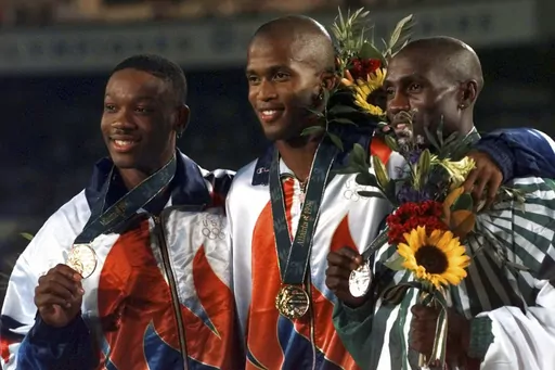 United States gold medalist Derrick Adkins is flanked by teammate and bronze medalist Calvin Davis, left, and silver medalist Samuel Matete of Zambia, right, after the 400 meter hurdle final at the 1996 Summer Olympic Games in Atlanta, Thursday, Aug. 1, 1996. Calvin Davis, the Olympic bronze medalist in the 400 hurdles at the 1996 Atlanta Games, has died. He was 51. The University of Arkansas, where he went to school, said Davis died Monday, May 1, 2023. No cause of death was given. (AP Photo/Ed
