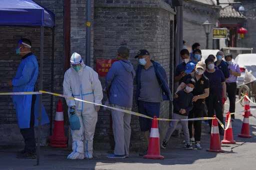 A worker in protective suit sprays disinfectant as residents line up for mass COVID test on Monday, May 16, 2022, in Beijing. Authorities say most of Shanghai has stopped the spread of the coronavirus in the community and fewer than 1 million people remain under strict lockdown. China's largest city is moving toward reopening as economic data showed the gloomy impact of China's "zero-COVID" policy. (AP Photo/Andy Wong)