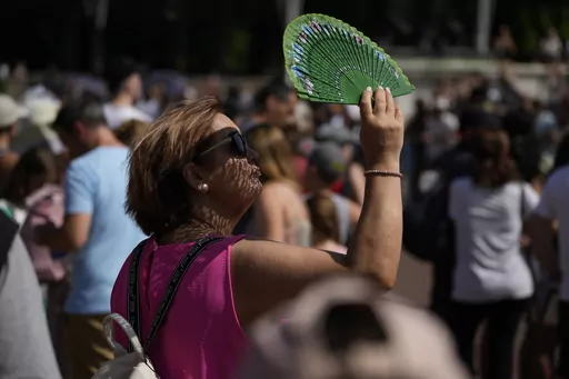 A tourist uses a fan to shade her face from the sun while waiting to watch the Changing of the Guard ceremony outside Buckingham Palace, during hot weather in London, July 18, 2022. Crushing temperatures that blanketed Europe during the summer of 2022 may have led to more than 61,000 heat-related deaths, according to a study published Monday, July 10, 2023. (AP Photo/Matt Dunham, File)