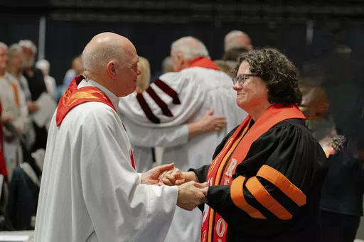 In this photo provided by the United Methodists of Eastern Pennsylvania, Rev. Dr. Beth Stroud, right, holds hands with Bishop John Schol after offering a prayer of blessing at the Wildwoods Convention Center, Wildwood, N.J., on Tuesday, May 21, 2024, as he prepares to retire in August. Twenty years ago, Stroud was defrocked as a pastor after telling her congregation that she was in a committed same-sex relationship. On Tuesday night, less than three weeks after the UMC repealed its anti-LGBTQ ba