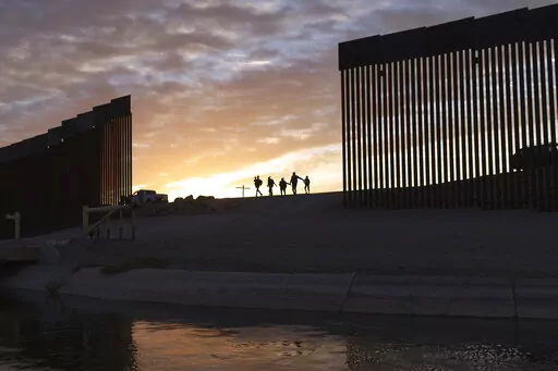 A pair of migrant families from Brazil passes through a gap in the border wall to reach the United States after crossing from Mexico in Yuma, Ariz., to seek asylum on June 10, 2021. The Biden administration may be ending asylum restrictions at the U.S.-Mexico border put in place to stop the spread of COVID-19, but the political and humanitarian challenges for the president may only get worse. (AP Photo/Eugene Garcia, File)