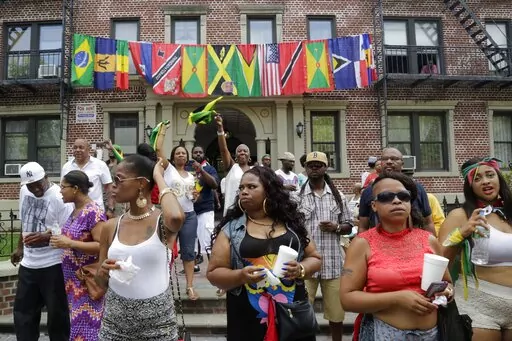 Flags representing Caribbean nations drape the front of a residential building as people gather outside to watch the annual West Indian Day Parade, celebrating Caribbean heritage, Sept. 1, 2014 in the Brooklyn borough of New York. A new report on Thursday, April 14, 2022 by Pew Research Center says a majority of Black Americans believe being Black is central to how they think about themselves and shape their identities, even as many have diverse experiences and come from various backgrounds. (AP