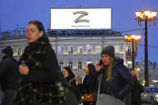 People walk past the letter Z, which has become a symbol of the Russian military, and a hashtag reading "We don't abandon our own" on an advertisement screen in St. Petersburg, Russia, Wednesday, March 9, 2022. (AP Photo)