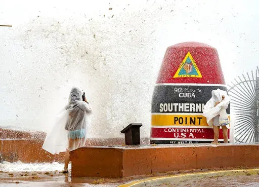 Visitors to the Southernmost Point buoy in Key West, Fla., brave the waves for photos as the island chain is under a tropical storm warning on Friday, June, 3, 2022. Tropical storm warnings were issued early Friday for much of the Florida peninsula, Cuba and the Bahamas as a system that battered Mexico moves through the Gulf of Mexico, bringing threats of heavy rain and wind for the weekend. (Rob O'Neal/The Key West Citizen via AP)