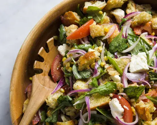 This image released by Milk Street shows a recipe for tomato, arugula and bread salad with fresh corn and mozzarella. (Milk Street via AP)