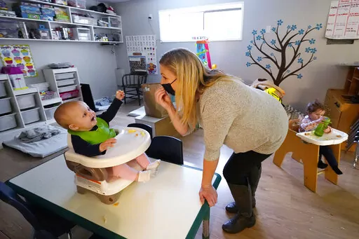 Amy McCoy signs to a baby about food as a toddler finishes lunch behind at her Forever Young Daycare facility, Monday, Oct. 25, 2021, in Mountlake Terrace, Wash. According to a report released by the Centers for Disease Control and Prevention on Tuesday, May 24, 2022, U.S. births bumped up in 2021, but the number of babies born was still lower than before the coronavirus pandemic. (AP Photo/Elaine Thompson, File)