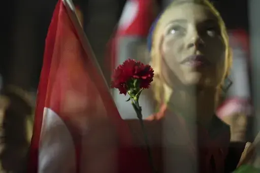 A protesters holds a flower as stand behind police barrier during a protest after Istanbul's Mayor Ekrem Imamoglu was arrested and sent to prison, in Istanbul, Turkey, Tuesday, March 25, 2025. (AP Photo/Francisco Seco)