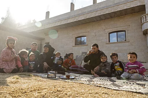 Milhem Daher, 35, drinks tea as he sits with his family outside his house in the village of Kasrat Srour, in the southeastern countryside of the Raqqa province, Syria, Monday, Feb. 7, 2022. Raqqa, the former de facto capital of the self-proclaimed IS caliphate and home to about 300,000, is now free, but many of its residents try to leave. Those with capital are selling their property to save up for the journey to Turkey. Those without money struggle to get by. (AP Photo/Baderkhan Ahmad)