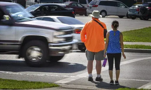 In this June 8, 2016, file photo, a maroon and silver truck drove, left, drives through the marked crosswalk in front of pedestrian volunteers Dave Passiuk and Nelsie Yang in St. Paul, Minn. Drivers of bigger vehicles such as pickup trucks and SUVs are more likely to hit pedestrians while making turns than drivers of cars, according to a new study. The research released Thursday, March 17, 2022, by the Insurance Institute for Highway Safety points to the increasing popularity of larger vehicles 