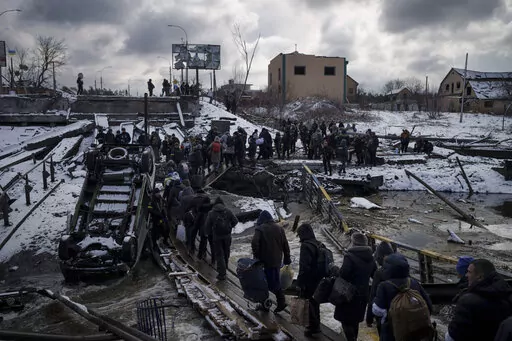 Ukrainians cross an improvised path under a destroyed bridge while fleeing Irpin, in the outskirts of Kyiv, Ukraine, Tuesday, March 8, 2022. As milestones go, the first anniversary of Russia's invasion of Ukraine is both grim and vexing. It marks a full year of killing, destruction, loss and pain felt even beyond the borders of Russia and Ukraine. (AP Photo/Felipe Dana, File)