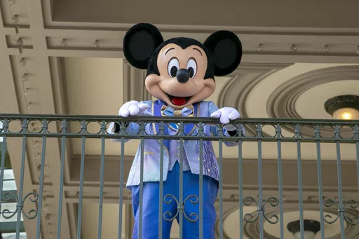 An actor dressed as Mickey Mouse greets visitors at the entrance to Magic Kingdom Park at Walt Disney World Resort, April 18, 2022, in Lake Buena Vista, Fla. Winnie the Pooh and Mickey Mouse have recently entered the public domain, making it possible for artists to use them freely. (AP Photo/Ted Shaffrey, File)
